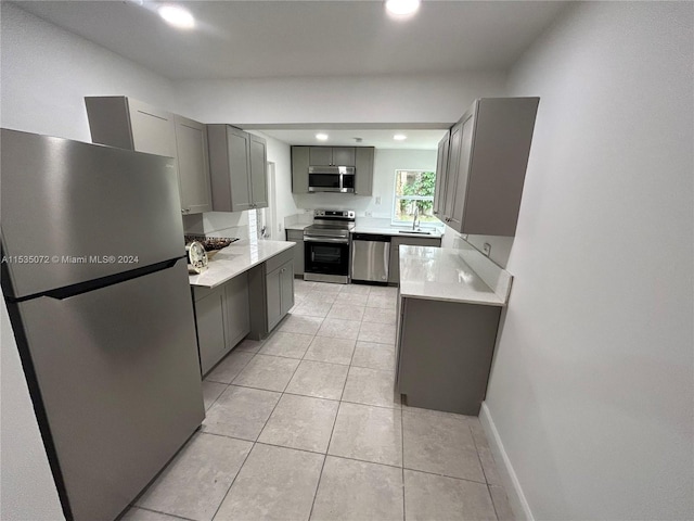 kitchen with appliances with stainless steel finishes, gray cabinets, sink, and light tile flooring