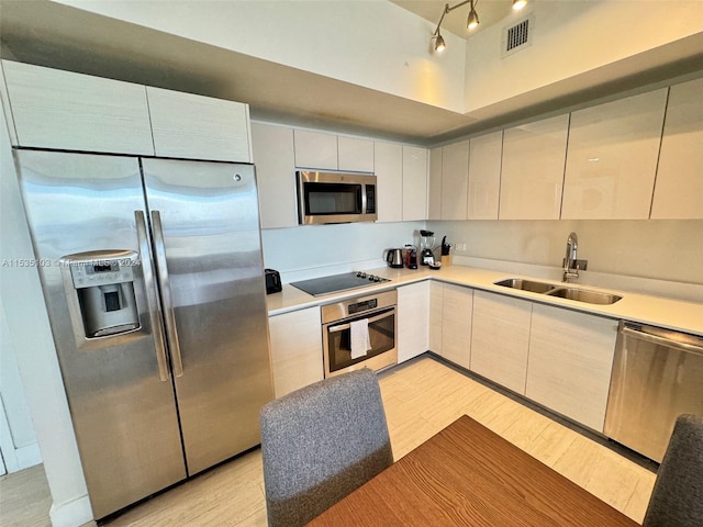 kitchen with appliances with stainless steel finishes, rail lighting, sink, and light wood-type flooring