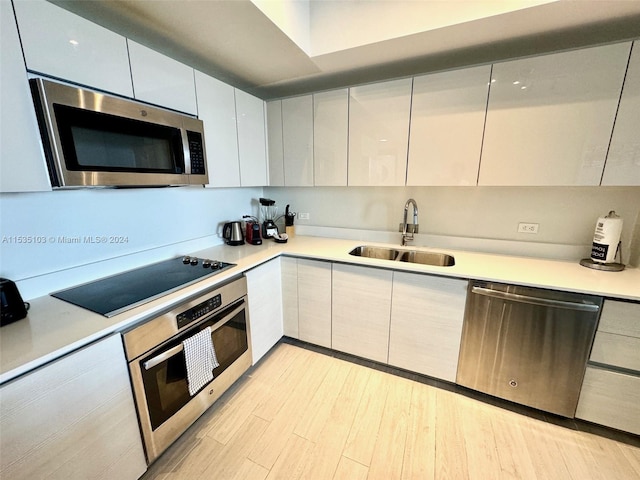 kitchen featuring white cabinets, light wood-type flooring, appliances with stainless steel finishes, and sink