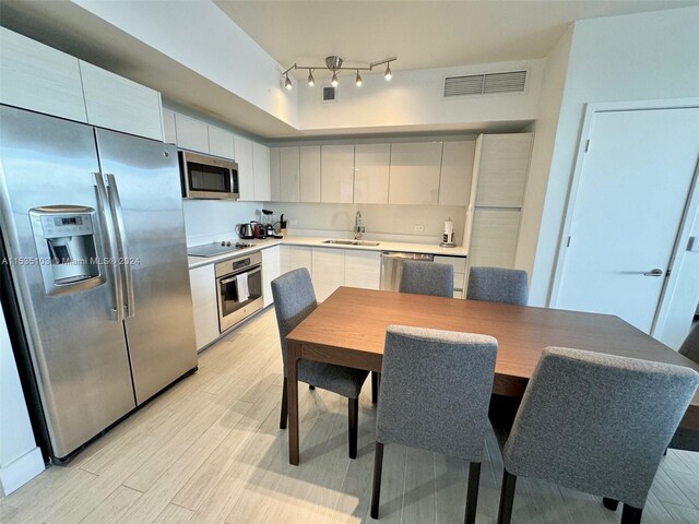 kitchen with light hardwood / wood-style flooring, white cabinetry, appliances with stainless steel finishes, track lighting, and sink