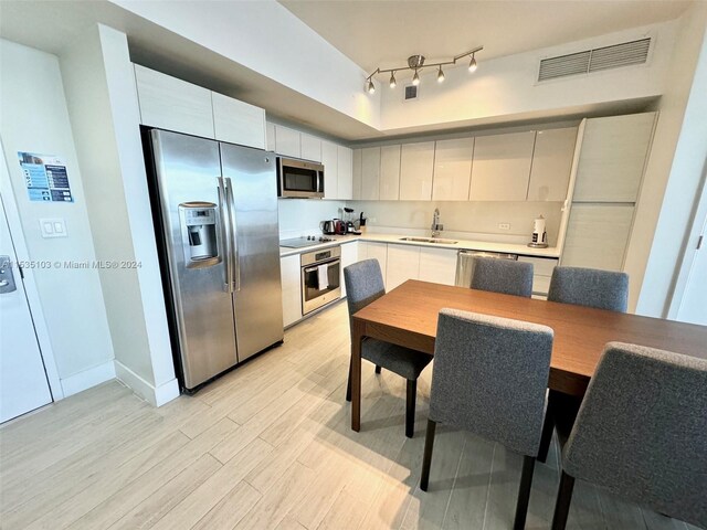 kitchen with rail lighting, light hardwood / wood-style flooring, appliances with stainless steel finishes, white cabinets, and sink