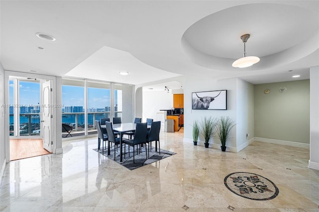 dining area featuring floor to ceiling windows, a raised ceiling, and a water view