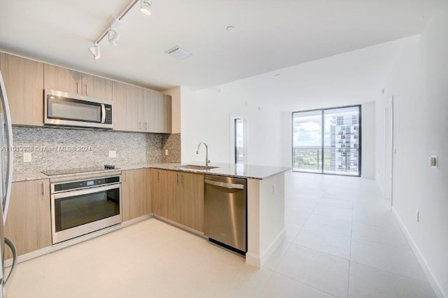 kitchen featuring stainless steel appliances, track lighting, light stone countertops, tasteful backsplash, and light brown cabinets