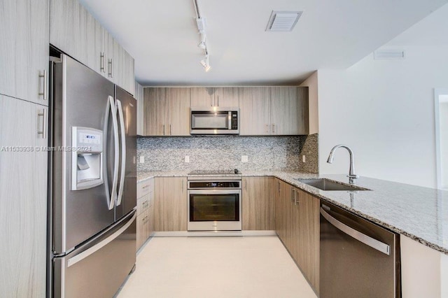 kitchen featuring sink, rail lighting, appliances with stainless steel finishes, light stone countertops, and tasteful backsplash