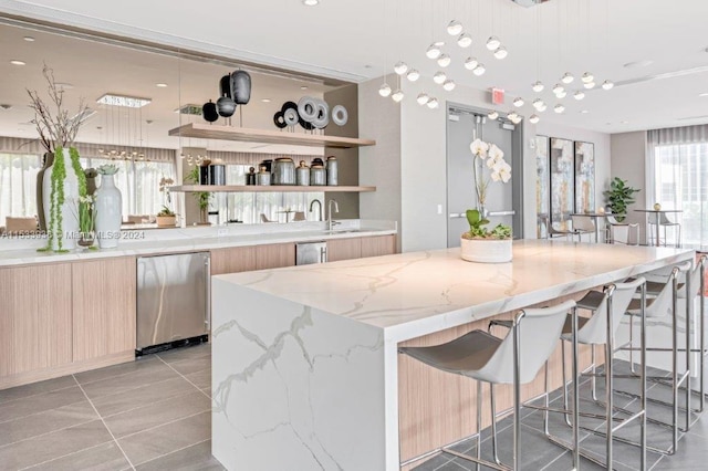 kitchen with light tile flooring, a center island, light stone counters, light brown cabinetry, and pendant lighting