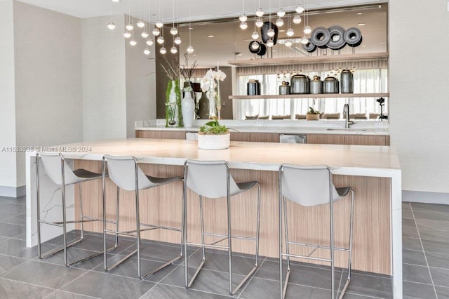 bar with pendant lighting, light stone countertops, dark tile flooring, dishwasher, and sink