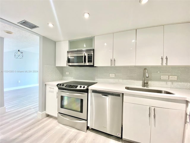 kitchen featuring white cabinets, backsplash, light wood-type flooring, and stainless steel appliances