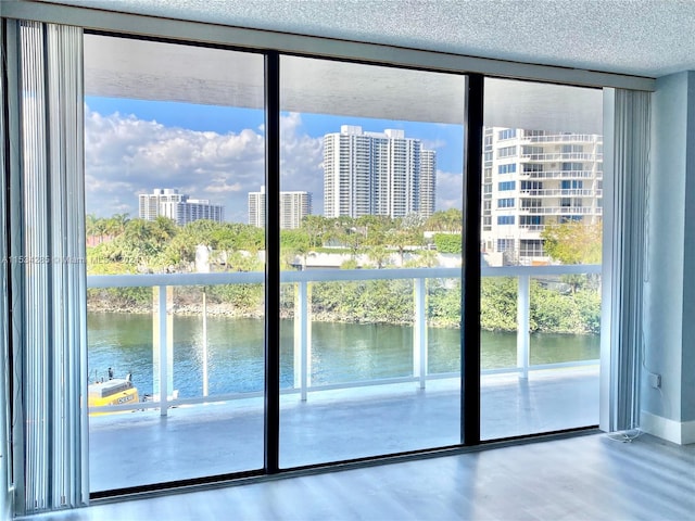 doorway with a water view, light hardwood / wood-style floors, a textured ceiling, and a wall of windows