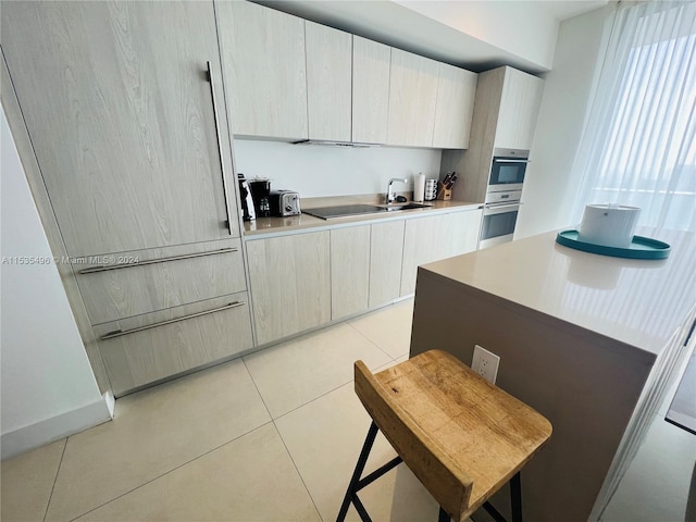 kitchen featuring double oven, a breakfast bar area, and light tile flooring