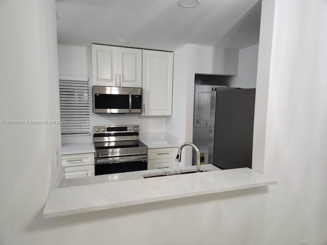 kitchen featuring white cabinetry, stainless steel appliances, sink, and light stone countertops