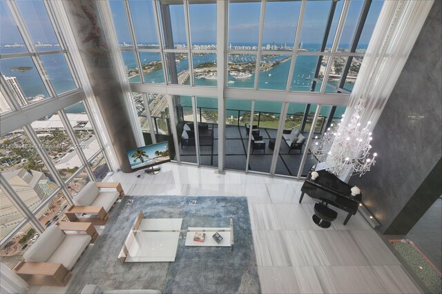 living room featuring a wall of windows, a chandelier, a towering ceiling, and a water view