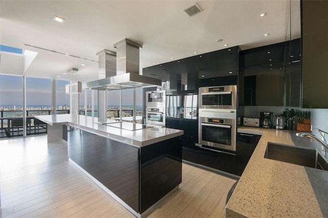 kitchen with light stone countertops, hanging light fixtures, sink, a kitchen island, and island exhaust hood