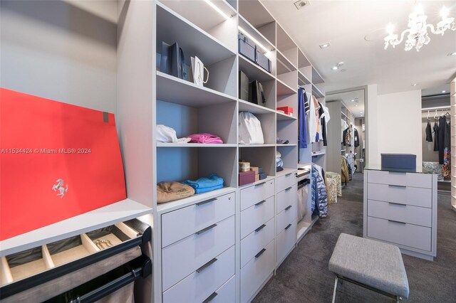 walk in closet with a notable chandelier and dark colored carpet