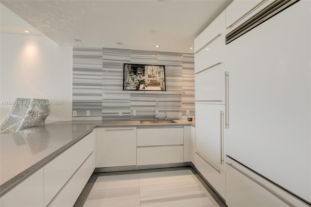 kitchen with backsplash, white built in refrigerator, sink, white cabinets, and light stone counters