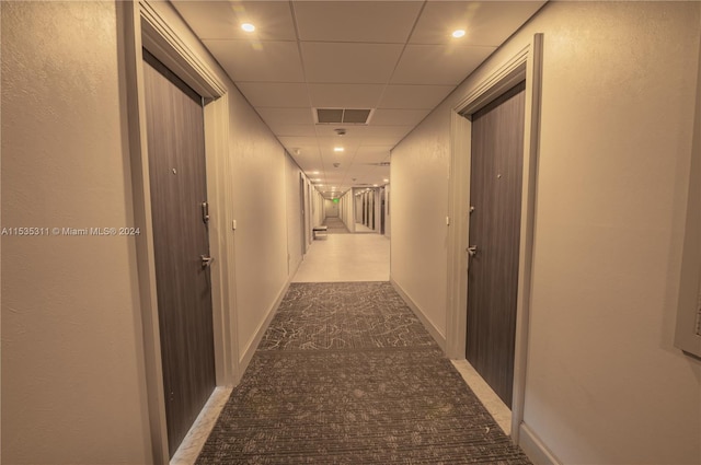 hall with a paneled ceiling and dark tile flooring