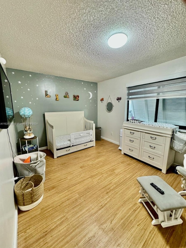 bedroom with light hardwood / wood-style floors, a textured ceiling, and a crib