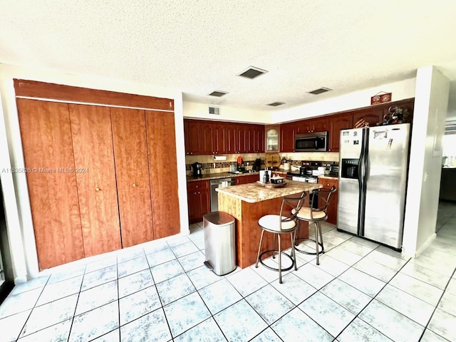 kitchen featuring a textured ceiling, light tile floors, a center island, a kitchen bar, and appliances with stainless steel finishes