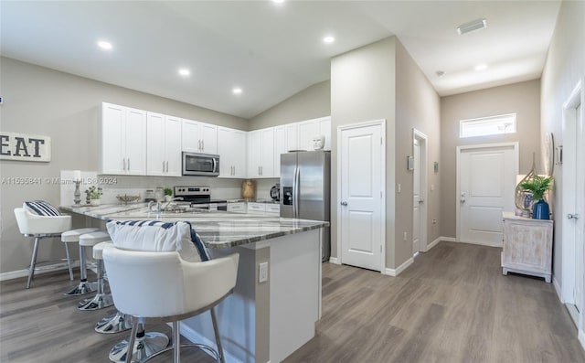 kitchen featuring appliances with stainless steel finishes, white cabinetry, light hardwood / wood-style floors, and a kitchen bar