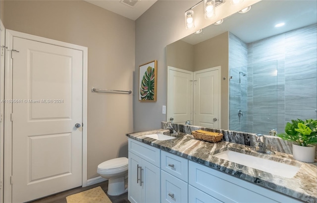 bathroom featuring oversized vanity, toilet, dual sinks, and walk in shower