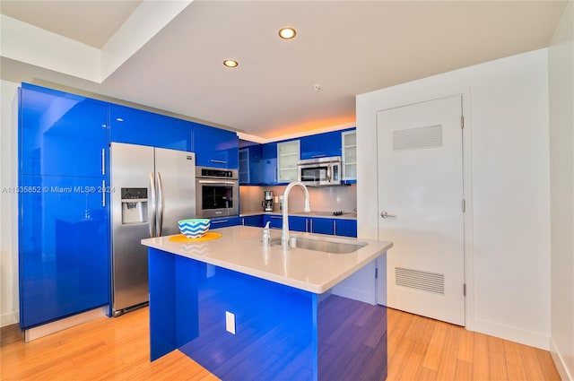 kitchen featuring appliances with stainless steel finishes, light hardwood / wood-style floors, a kitchen bar, and a kitchen island with sink