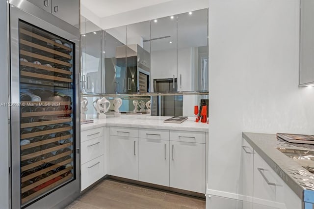 kitchen with wood-type flooring, light stone counters, wine cooler, and white cabinetry