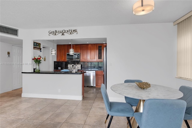 kitchen featuring tasteful backsplash, stainless steel appliances, decorative light fixtures, light tile flooring, and a textured ceiling