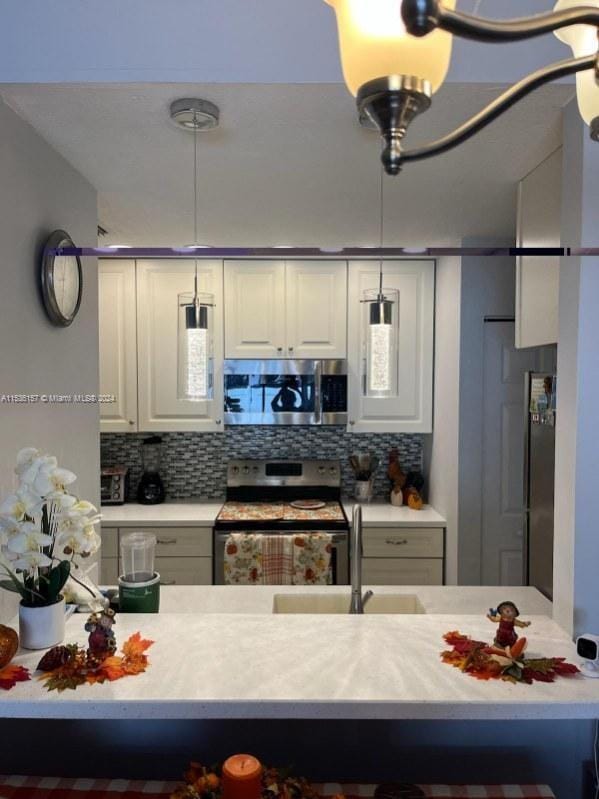 kitchen featuring a chandelier, decorative light fixtures, appliances with stainless steel finishes, white cabinets, and backsplash