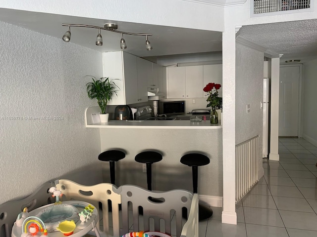 kitchen with white cabinets, ornamental molding, light tile floors, and rail lighting