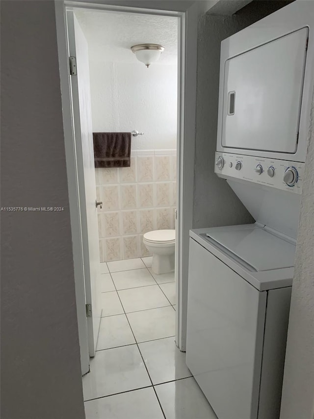 bathroom featuring tile flooring, tile walls, toilet, and stacked washing maching and dryer