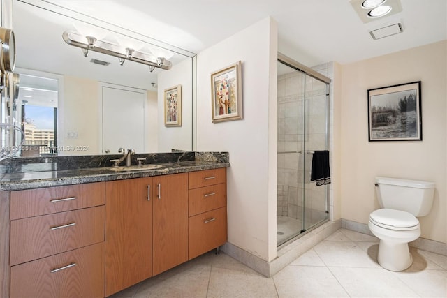 bathroom with tile floors, toilet, vanity, and a shower with shower door