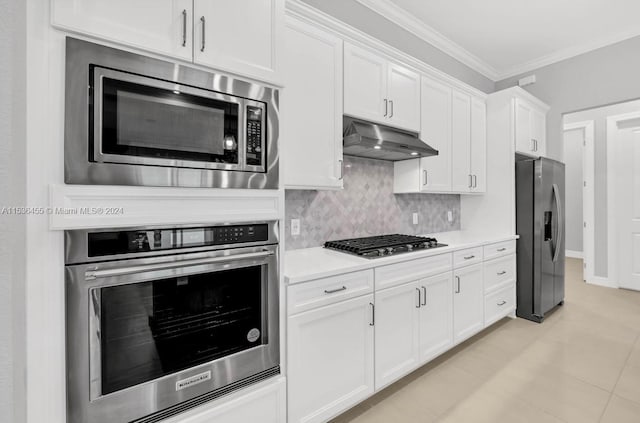 kitchen with backsplash, light tile flooring, appliances with stainless steel finishes, white cabinets, and crown molding