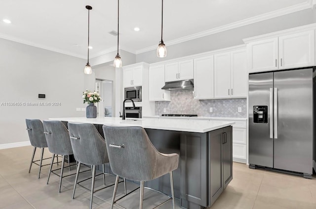 kitchen with hanging light fixtures, appliances with stainless steel finishes, a center island with sink, a breakfast bar area, and ornamental molding