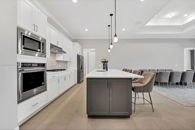 kitchen featuring a breakfast bar area, appliances with stainless steel finishes, white cabinetry, hanging light fixtures, and a kitchen island with sink