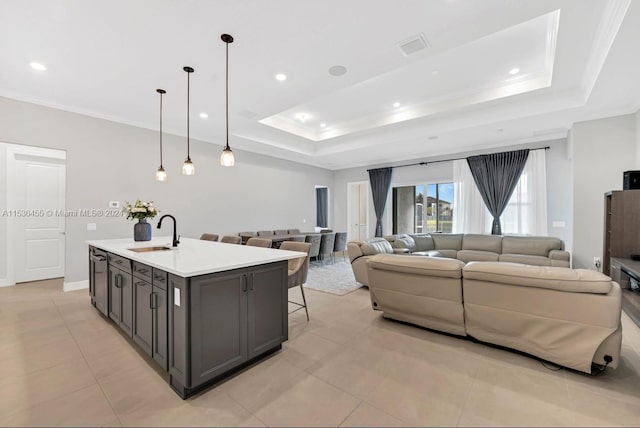 kitchen featuring sink, light tile floors, hanging light fixtures, a center island with sink, and a tray ceiling