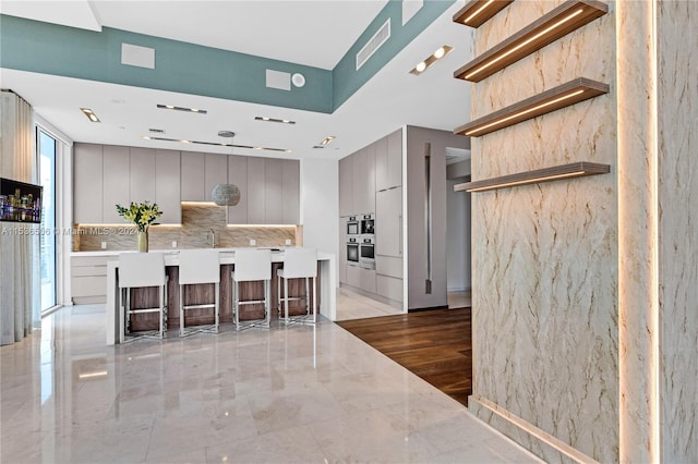 kitchen with gray cabinetry, oven, tasteful backsplash, and a kitchen bar