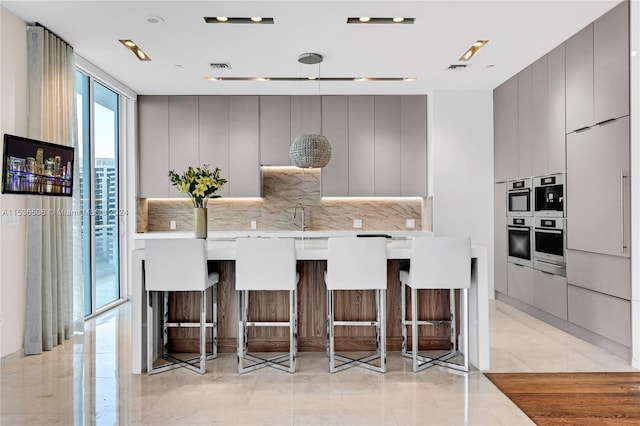 kitchen with backsplash, hanging light fixtures, a kitchen bar, sink, and light tile floors