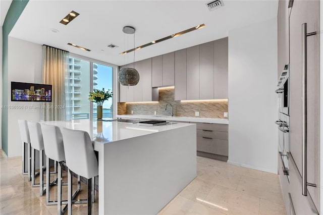 kitchen with an island with sink, backsplash, light tile floors, hanging light fixtures, and a breakfast bar