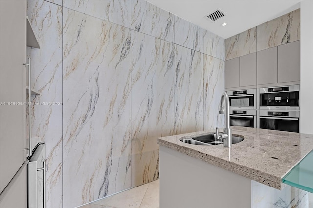 kitchen featuring tile walls, sink, double oven, and light stone countertops