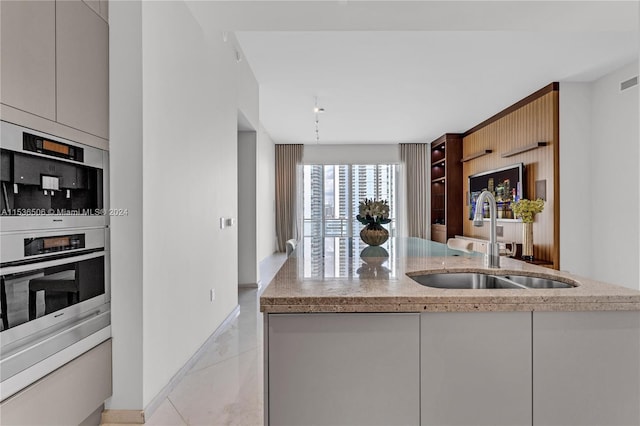 kitchen with light stone counters, light tile flooring, gray cabinetry, sink, and stainless steel double oven