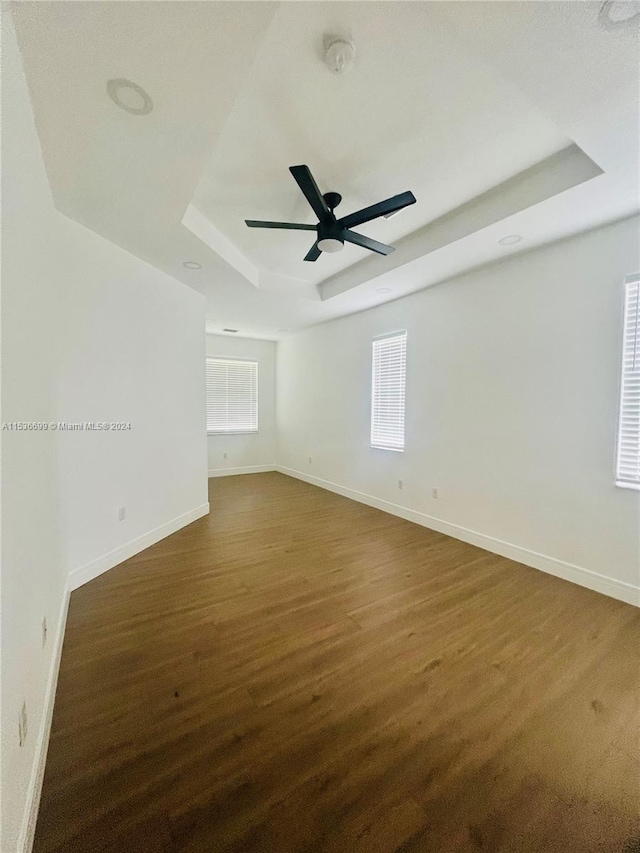 spare room with dark wood-type flooring, a raised ceiling, and ceiling fan