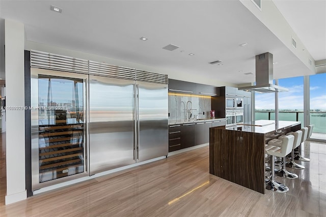 kitchen featuring a kitchen island with sink, a kitchen breakfast bar, light wood-type flooring, island range hood, and built in appliances