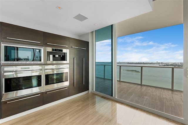 kitchen with light stone counters, light hardwood / wood-style flooring, double oven, black microwave, and dark brown cabinetry