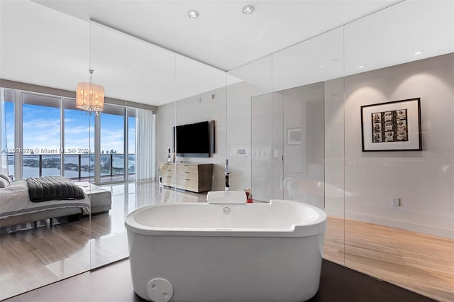 bathroom featuring a wall of windows, wood-type flooring, a water view, a bath to relax in, and a chandelier