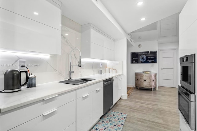 kitchen with light wood-type flooring, backsplash, stainless steel dishwasher, sink, and white cabinetry