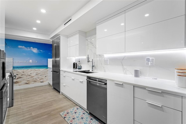 kitchen featuring light stone countertops, sink, light hardwood / wood-style floors, white cabinets, and appliances with stainless steel finishes