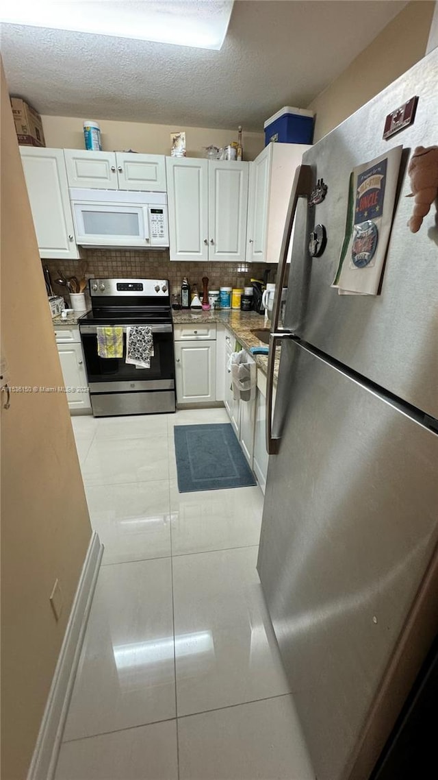 kitchen with light tile patterned floors, backsplash, stainless steel appliances, and white cabinets