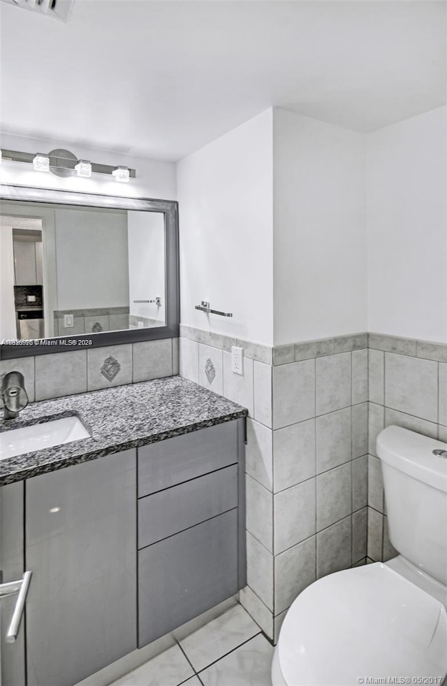 bathroom featuring tile walls, vanity with extensive cabinet space, tile floors, and toilet