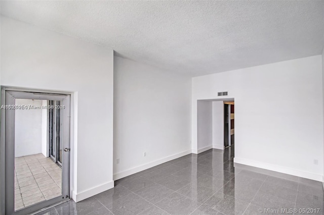 unfurnished room featuring a textured ceiling and dark tile flooring