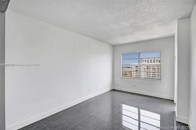 spare room featuring a textured ceiling and dark tile flooring