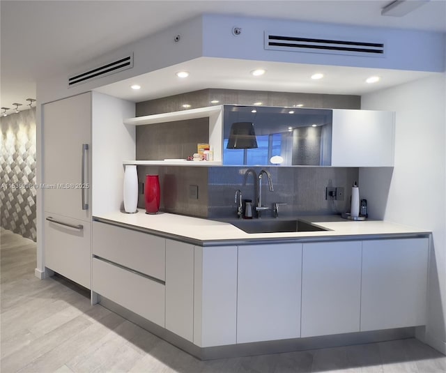 kitchen with white cabinets, decorative backsplash, light hardwood / wood-style floors, and sink